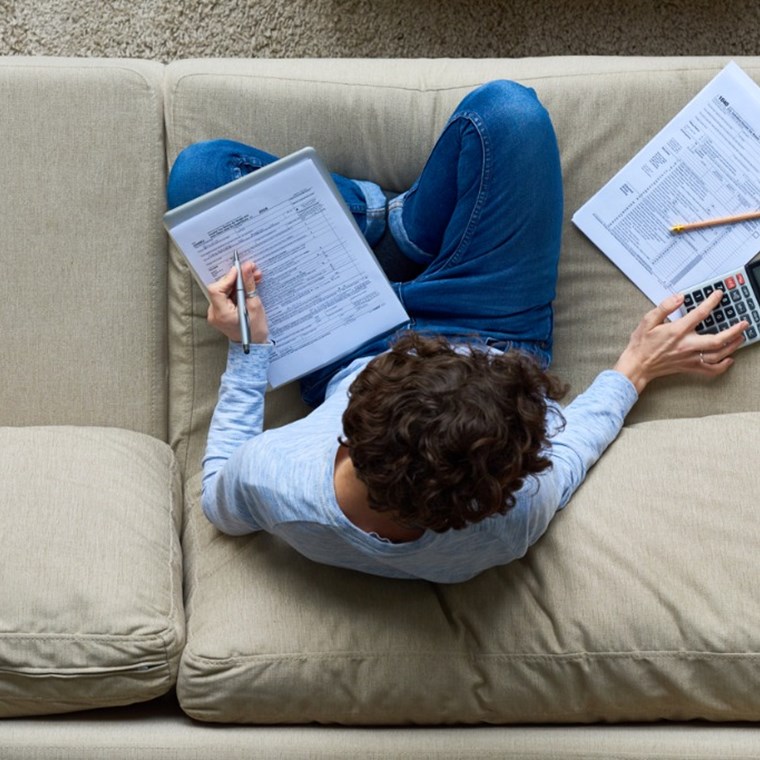 man filing tax return on couch with calculator